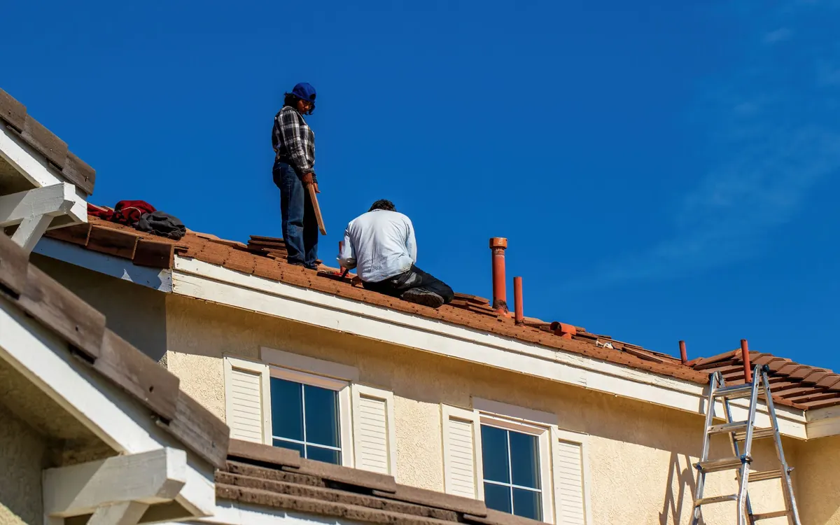 Two roofers working on a house roof on a clear day