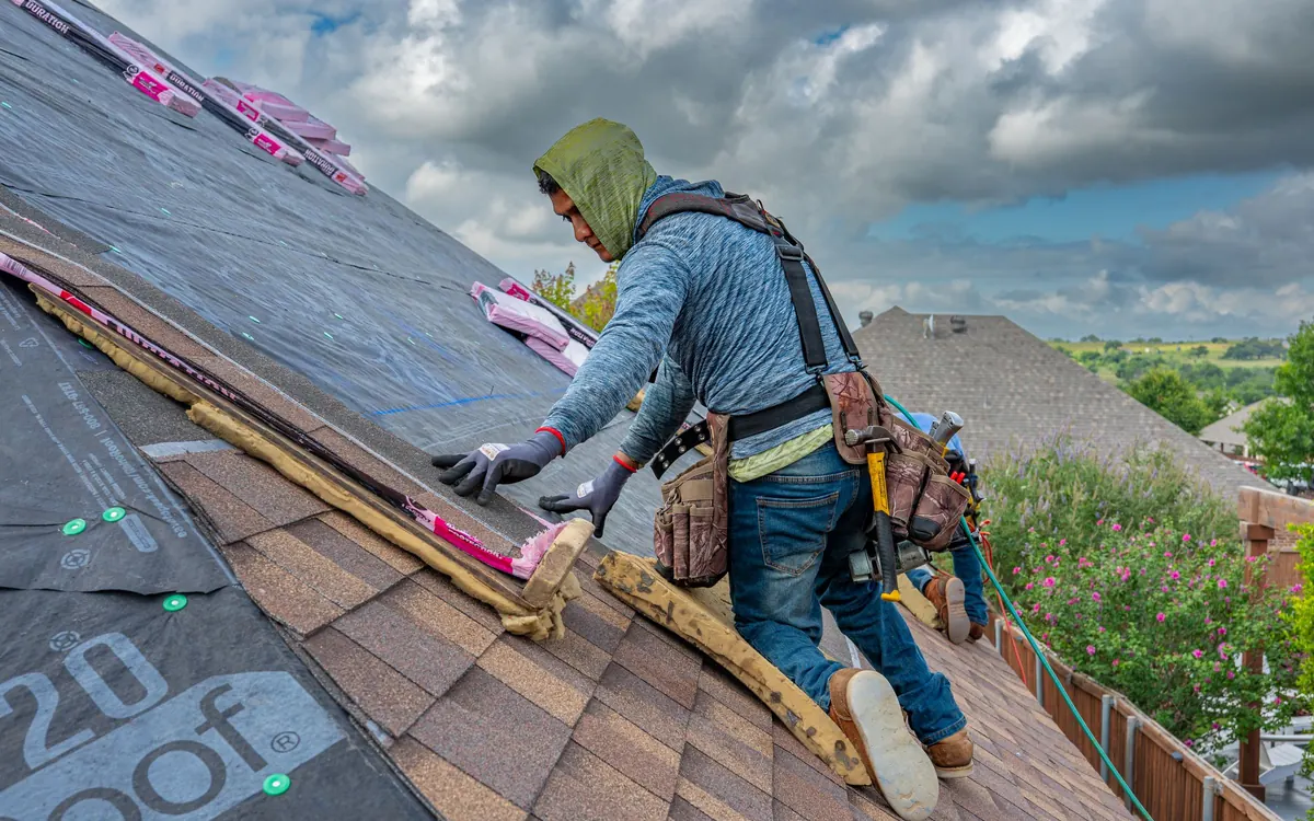 Roofer on a roof bracket installing shingles on a steep roof