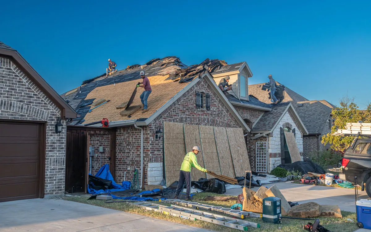 Roofing crew replacing the roof on a brick house, with tarps protecting the yard