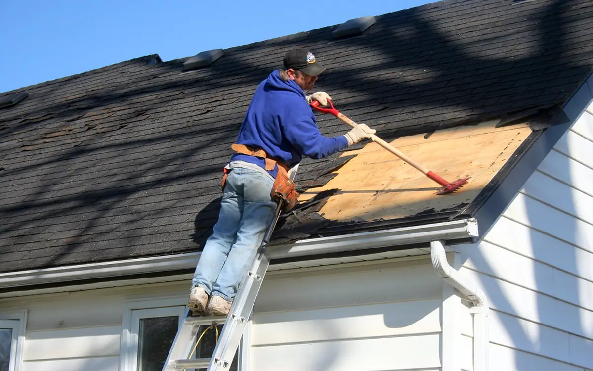 Roofer on a ladder removing old shingles to expose the roof deck