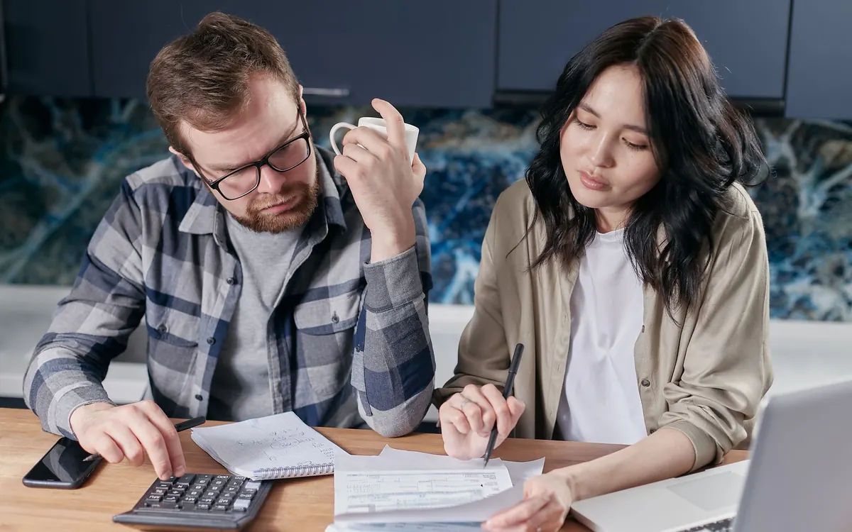 Couple reviewing bills and paperwork with a calculator at a kitchen table