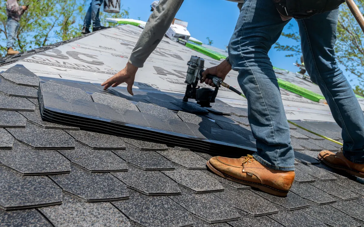 Roofer using a nail gun to fasten asphalt shingles