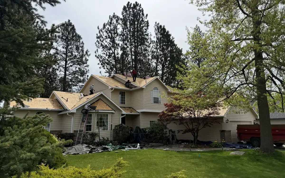 Roofing crew tearing off an old roof on a two-story home among pine trees