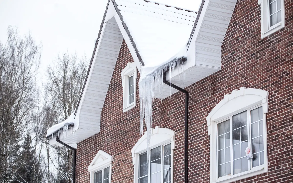 Brick house with snow on the roof and icicles hanging from the gutters
