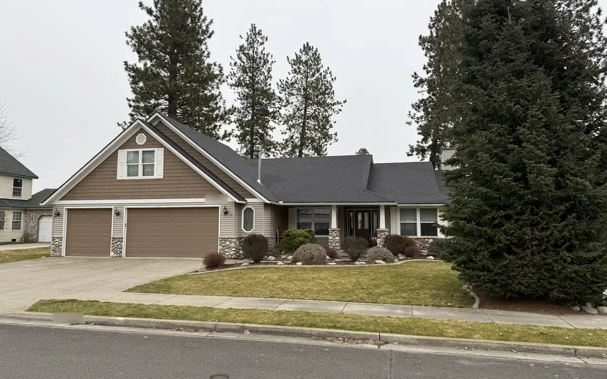 Single-story home with a dark architectural shingle roof, a three-car garage, and tall pine trees