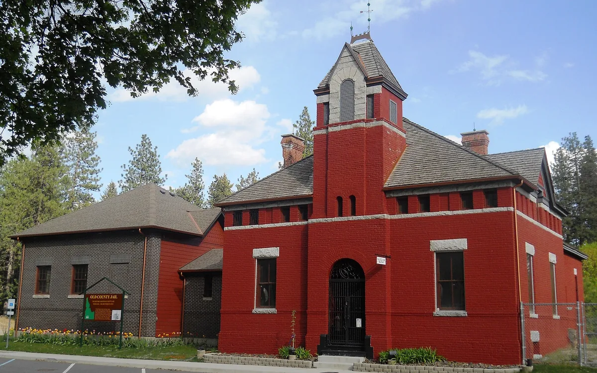 The historic Old Kootenai County Jail museum in Rathdrum, a red brick building with gray shingle roofs and a bell tower