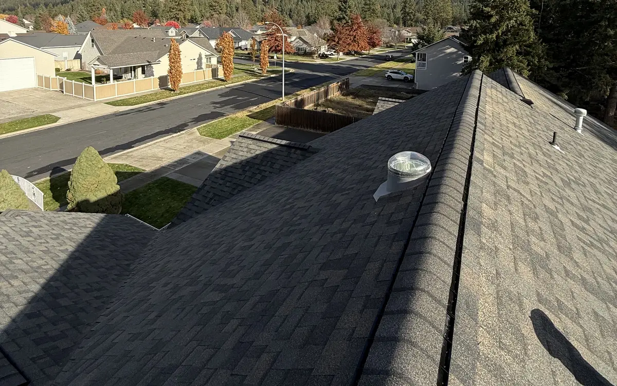 View along the ridge of an architectural shingle roof with a ridge vent and a tubular skylight, with the inspector's shadow on the shingles