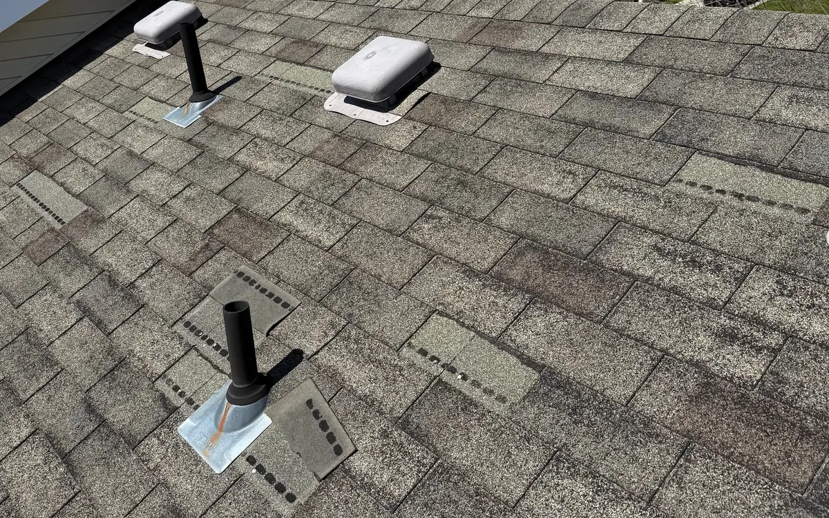 Wind-damaged asphalt shingle roof with missing shingle tabs around the vents, exposing the sealant strips underneath